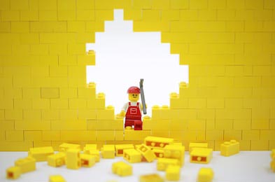 Строитель лего в красном костюме рушит желтую стену 