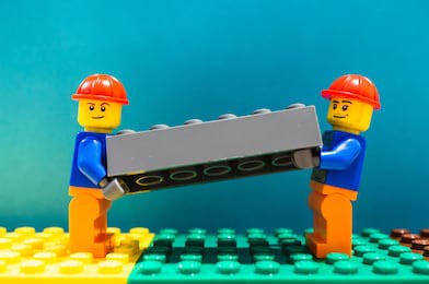 Два строителя Lego поднимают пластиковый кирпич
