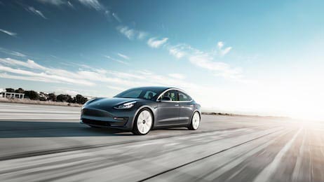 Серый Tesla Model 3 едет на закате