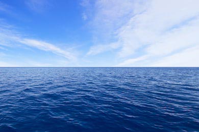 Синий спокойный океан на фоне голубого неба с тучами