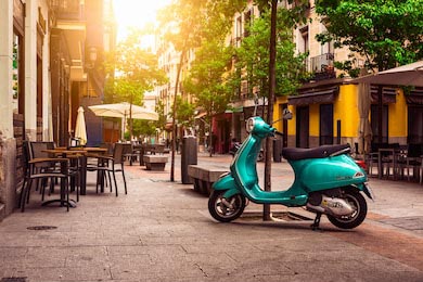Скутер Веспа на улице у столиков кафе в Мадриде